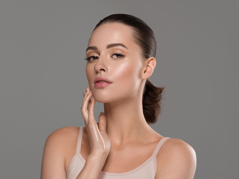 Smiling woman with clear skin touching her cheek, showcasing healthy and radiant complexion.