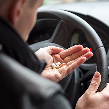 man holding pills behind the wheel