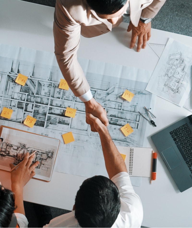 Men shaking hands over construction blueprints
