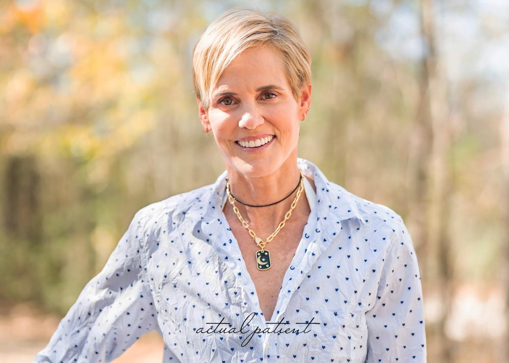 Smiling woman with short blonde hair wearing a white blouse outdoors, labeled as actual patient
