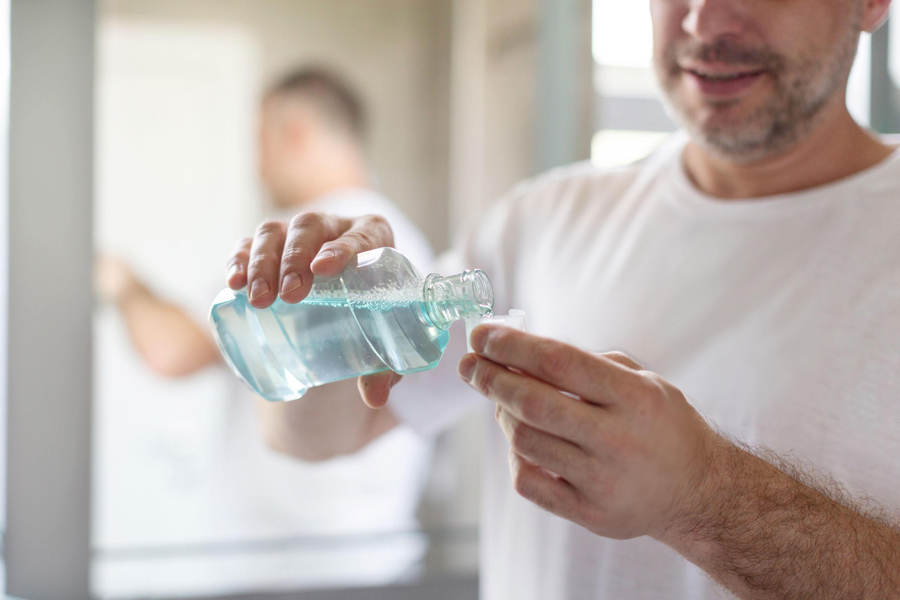 man pouring cup of mouthwash