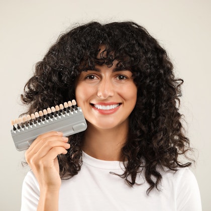 woman smiling while holding up shade matcher