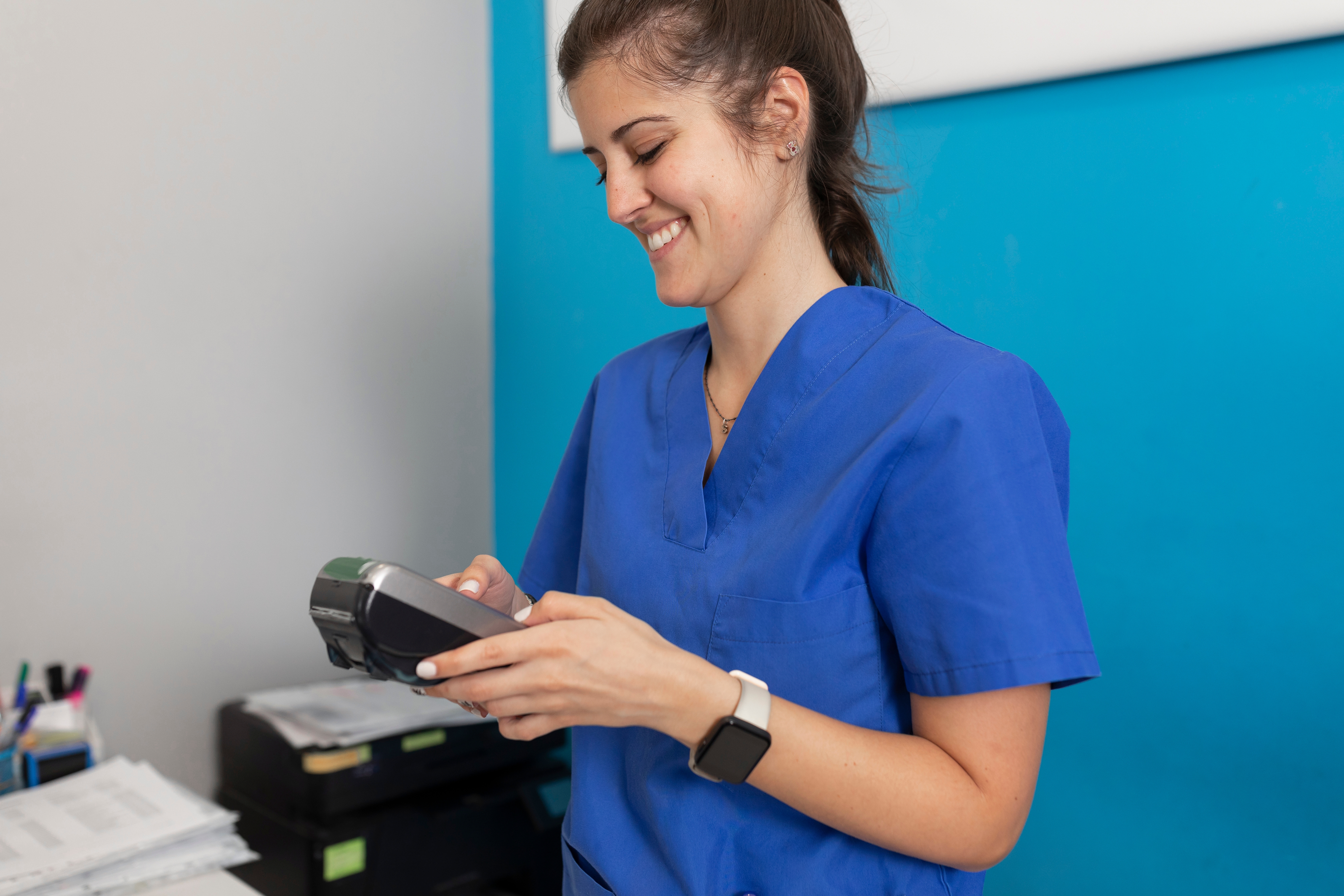 Smiling dental team member in blue scrubs using a payment terminal