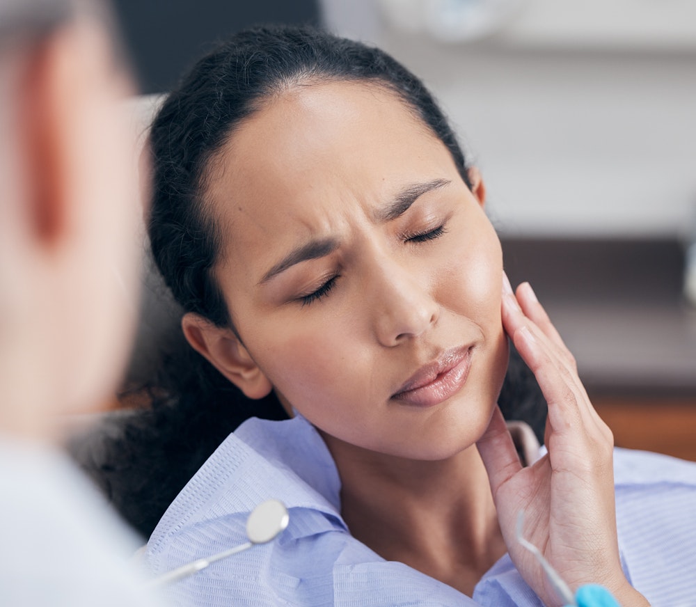 Woman in dental chair wincing and touching her jaw in pain