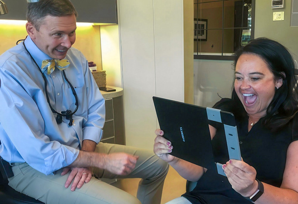 Elated patient looking at her smile in the mirror next to Dr. Thomas