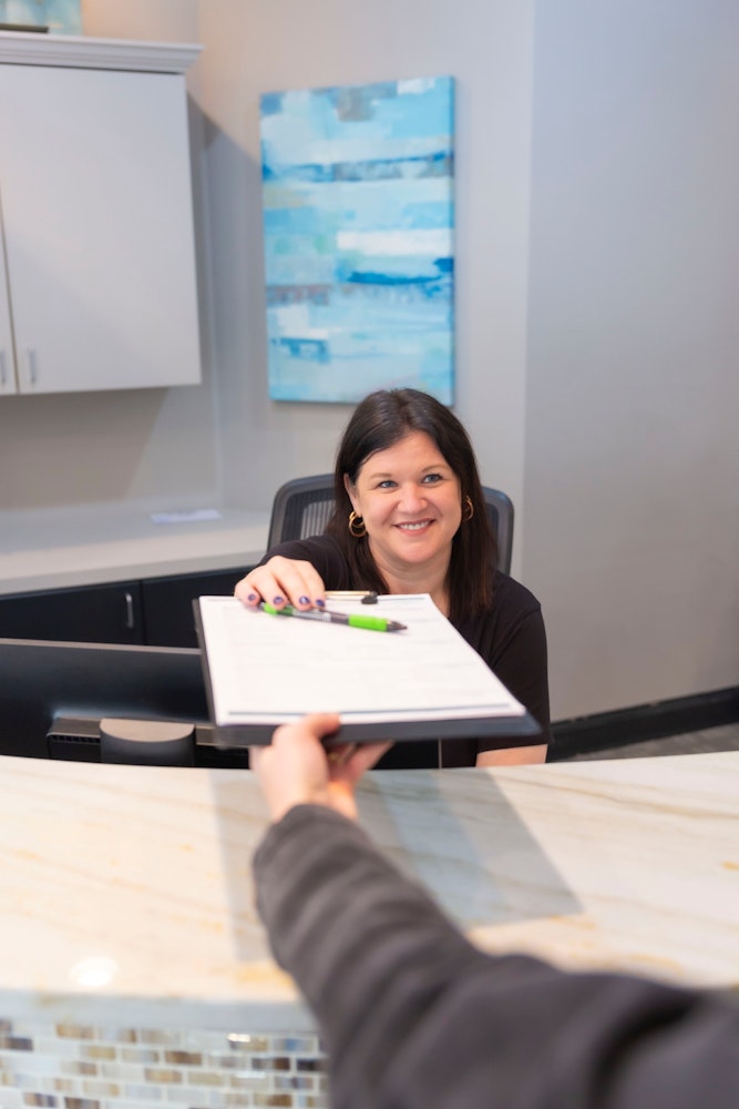 Front desk staff member handing paperwork to a patient at the reception desk of a dental office.