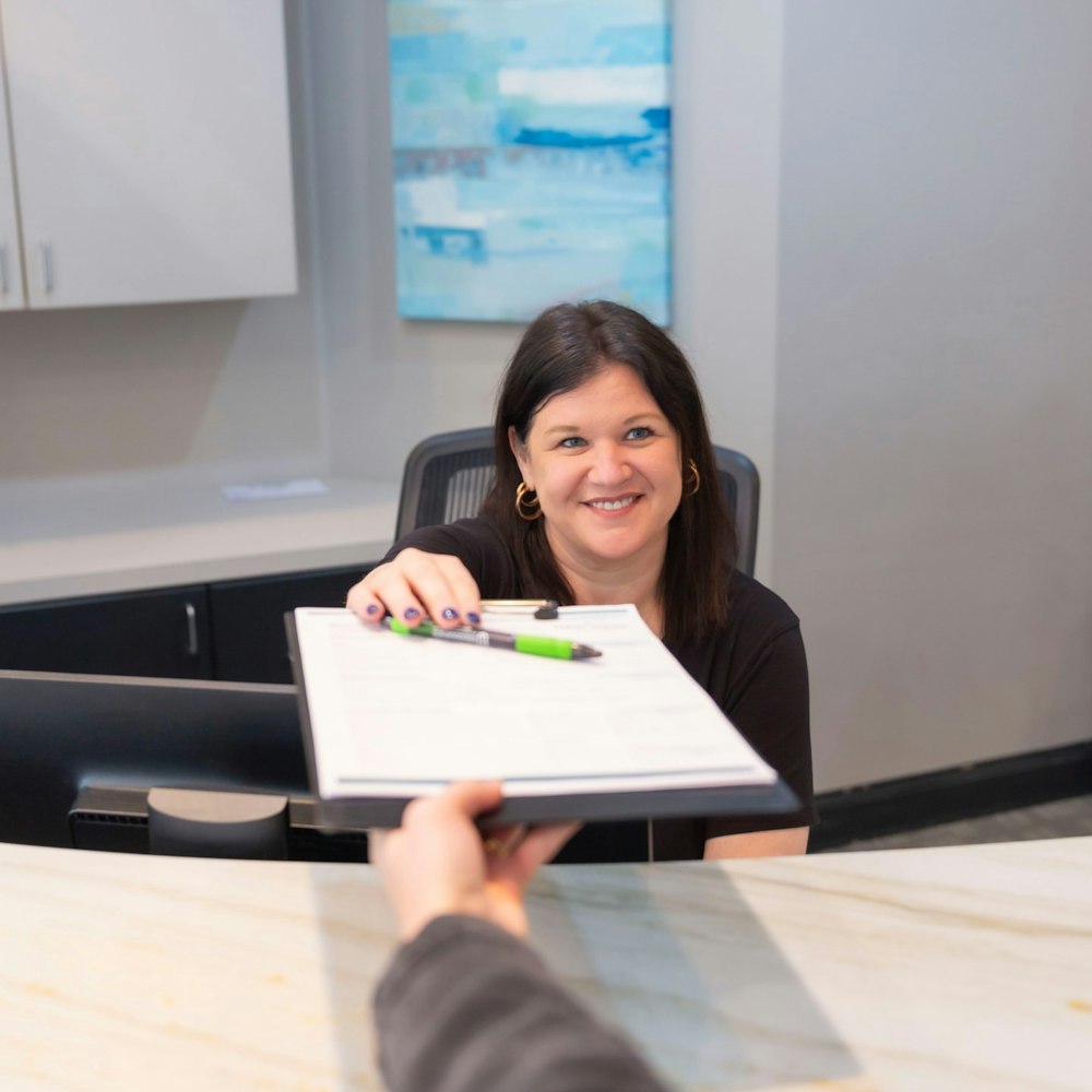 Front desk staff member handing paperwork to a patient at the reception desk of a dental office.