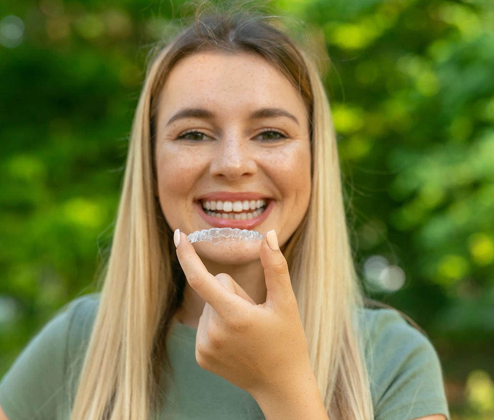 Smiling woman holding invisalign up to the camera