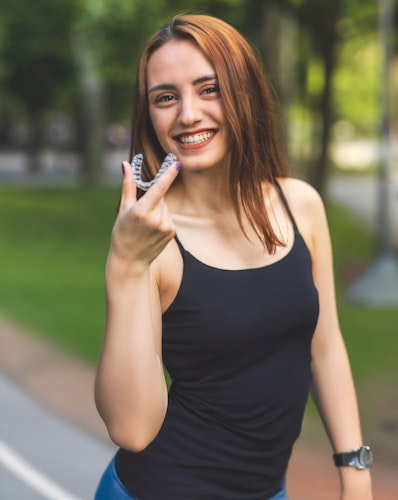 Smiling woman holding clear aligner