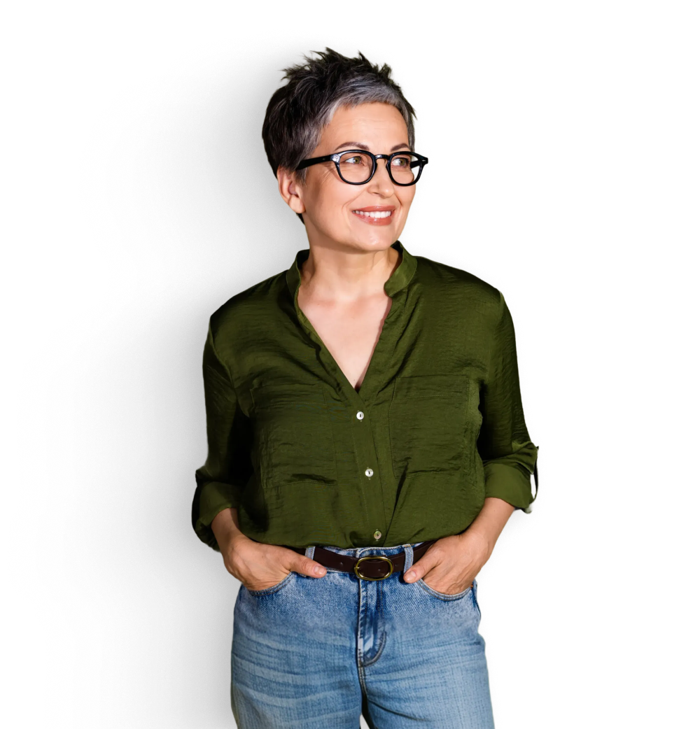 Smiling woman with short gray hair and glasses wearing a green blouse and jeans, standing with hands in pockets