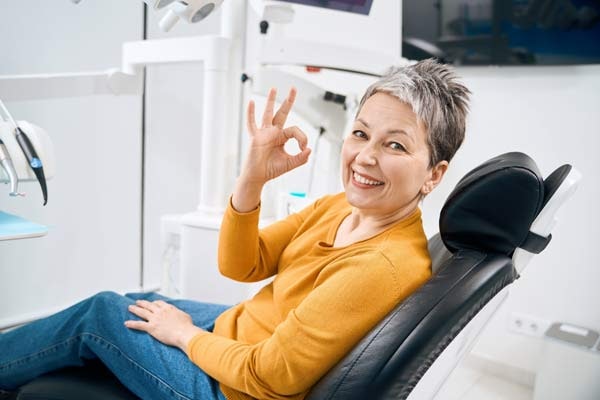 woman in dental chair holding up the "ok" sing