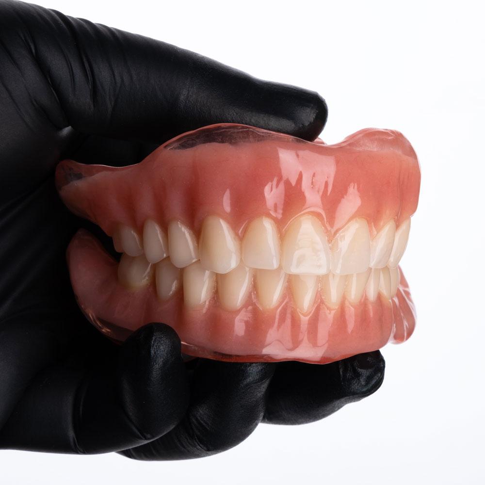 Gloved hand holding a traditional denture set