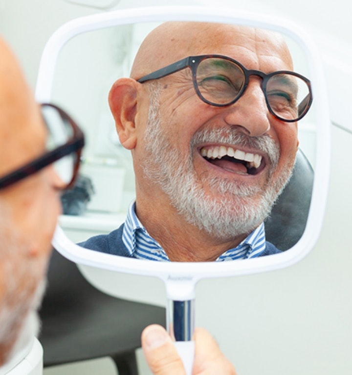 Happy dental implant patient looking in a hand mirror