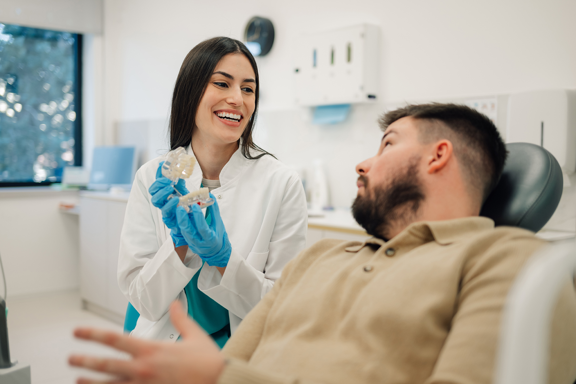Dentist wearing gloves showing a dental model to a man seated in a dental chair.