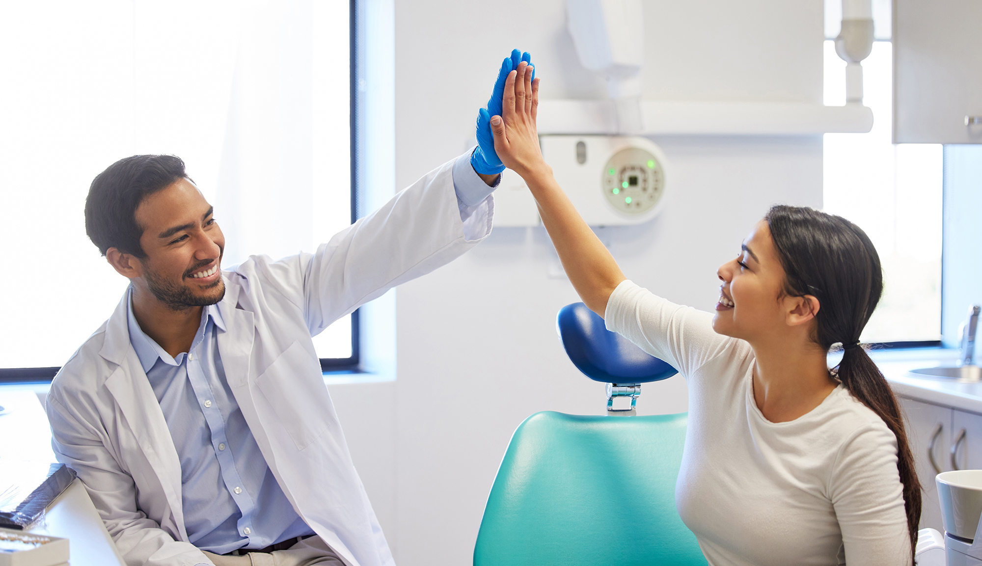 Dentist and patient smiling and giving a high five in a dental exam room.