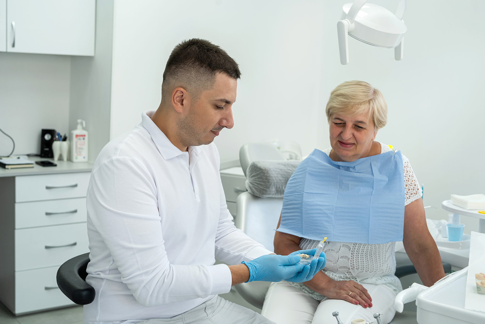 Dentist showing a dental model to an older woman during a consultation in a dental office.