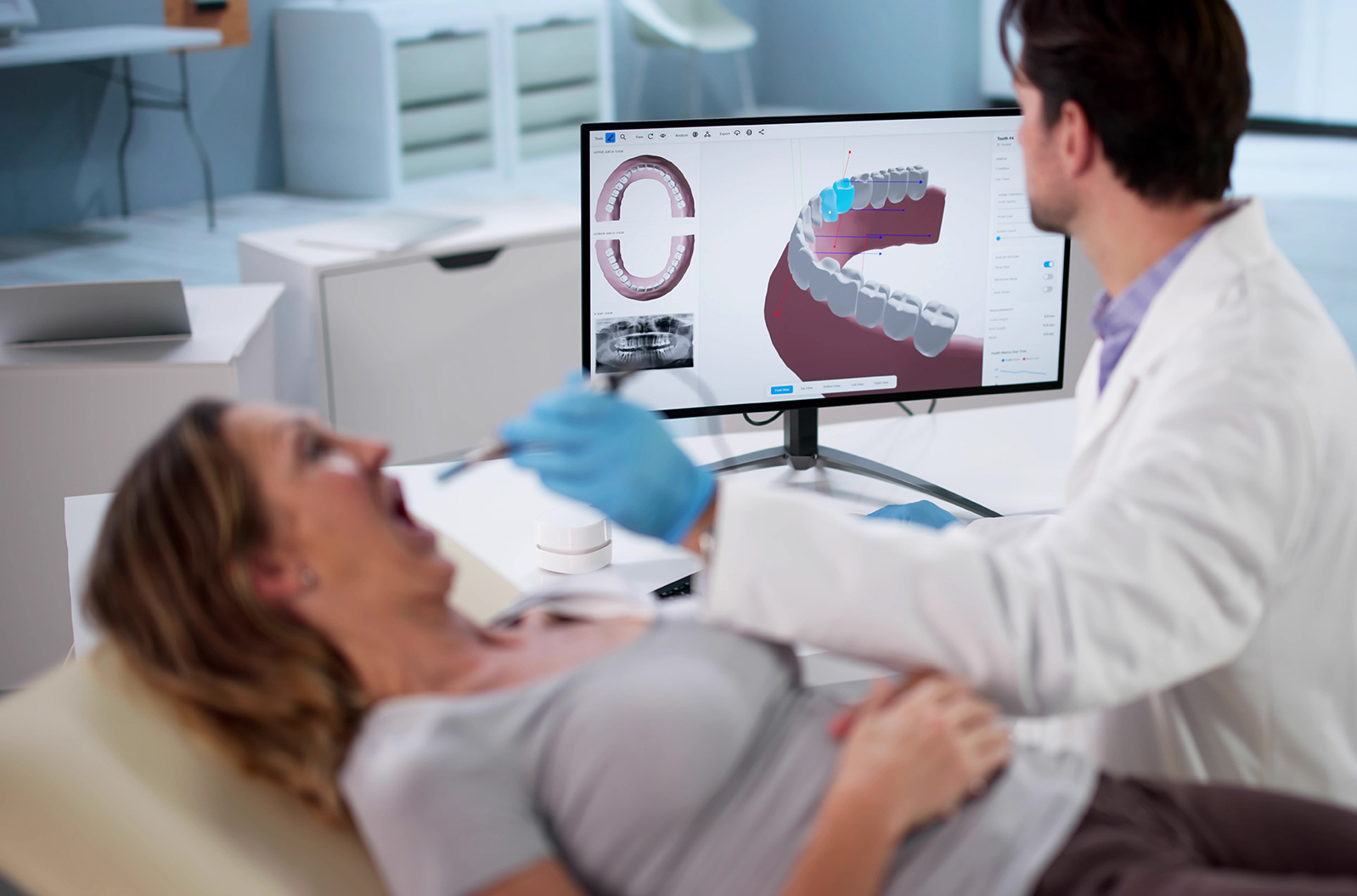 Dentist examining a patient’s teeth while a 3D dental scan is displayed on a computer monitor.