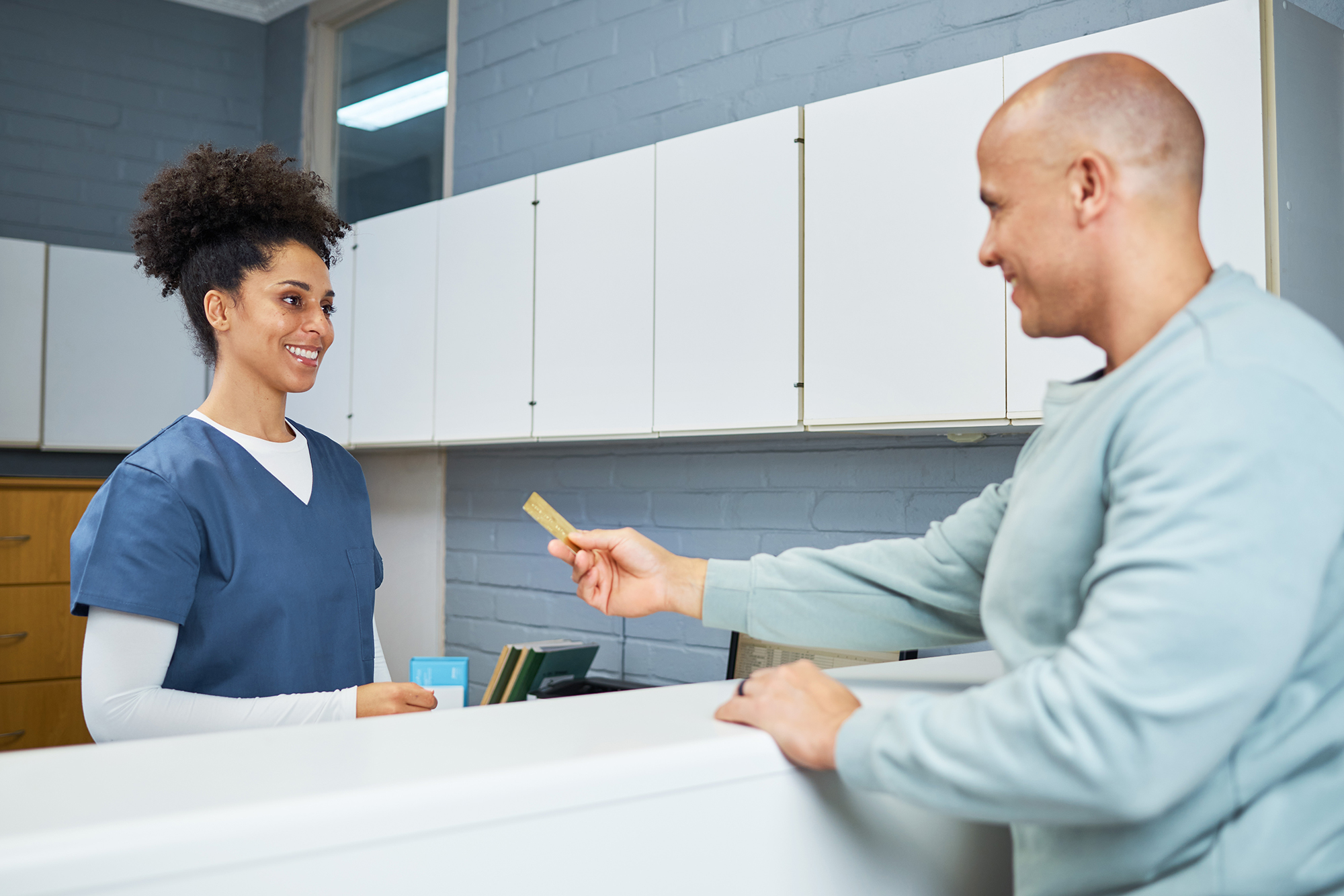 Patient handing a credit card to a receptionist at the front desk of a dental office.