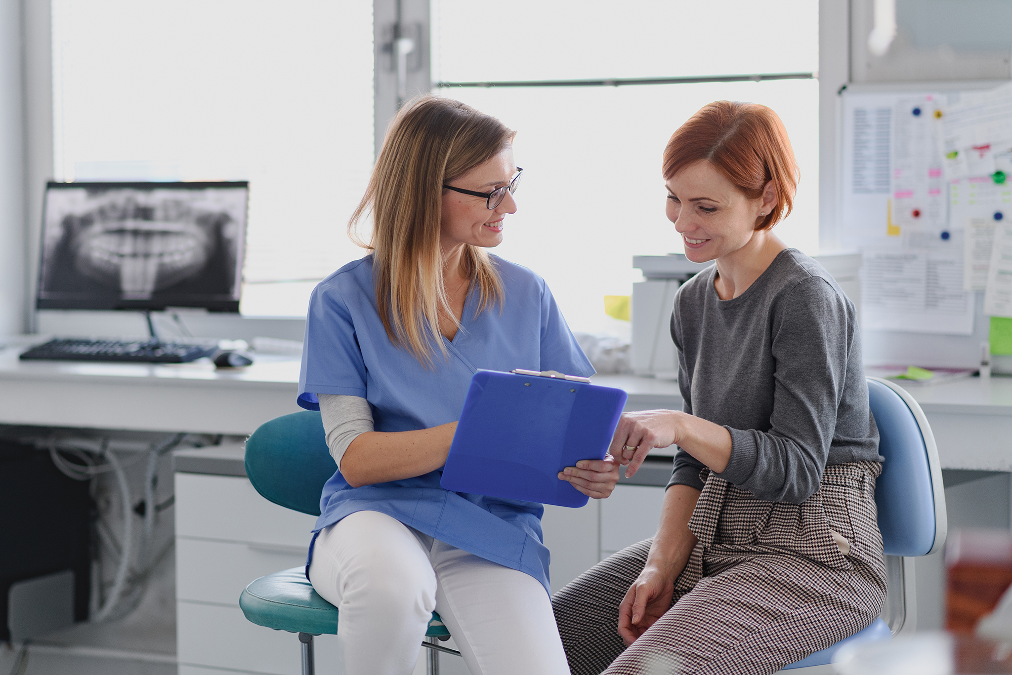 Dental professional reviewing information on a clipboard with a patient in a consultation room.