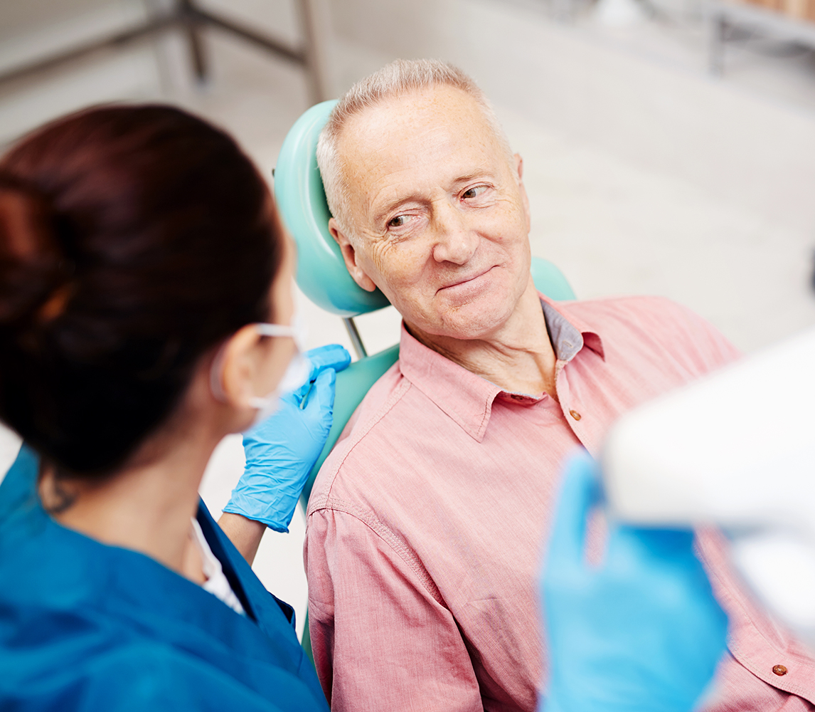 Dentist pointing to a dental model while speaking with a smiling woman seated in a dental chair.