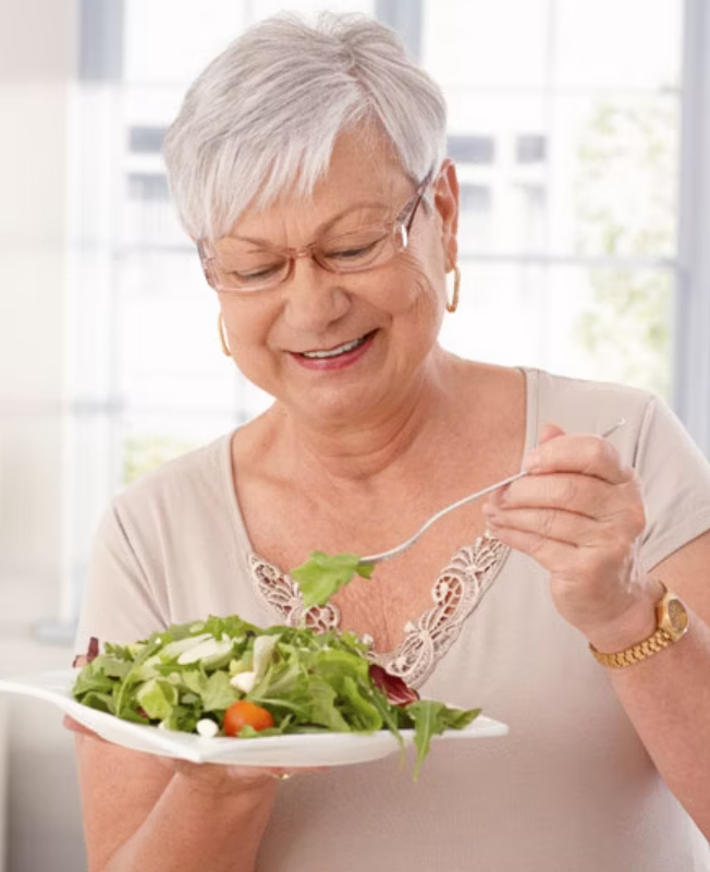older woman easting a salad smiling