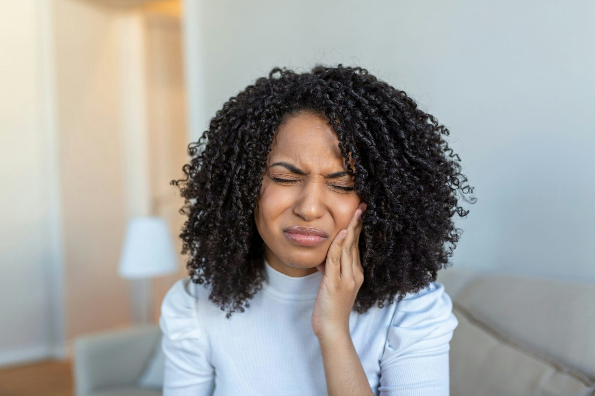 woman with curly hair holding her jaw in discomfort
