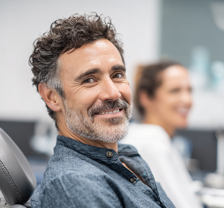Middle-aged man with salt-and-pepper hair smiling while seated in a dental chair.
