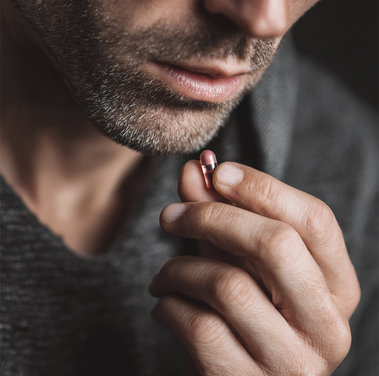 Close-up of man holding a red capsule pill near his lips.