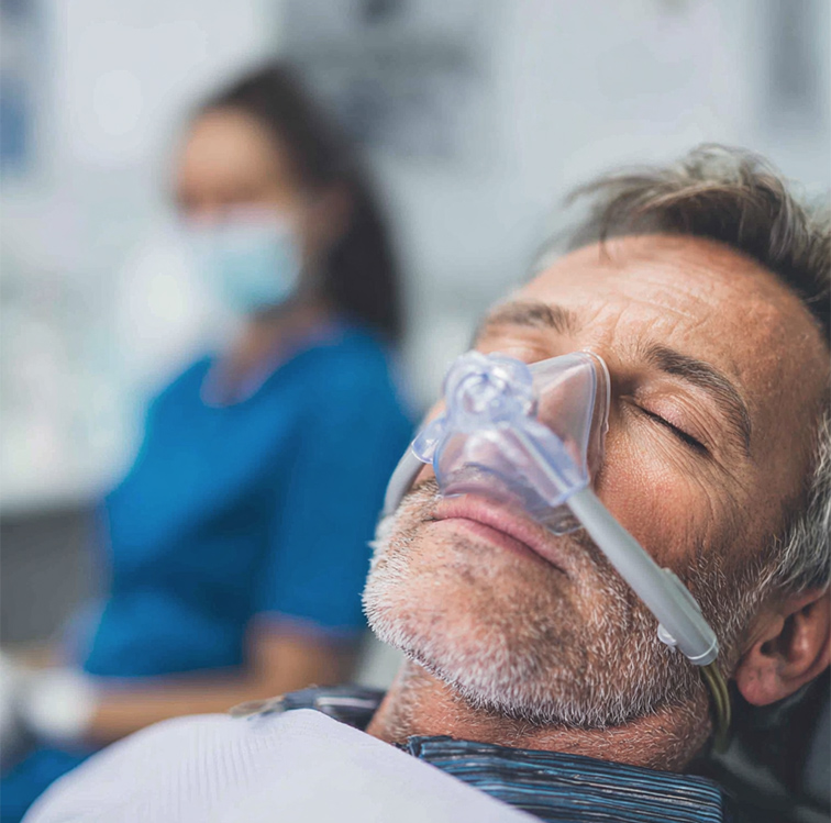Man with gray hair receiving nitrous oxide sedation in a dental chair, eyes closed.