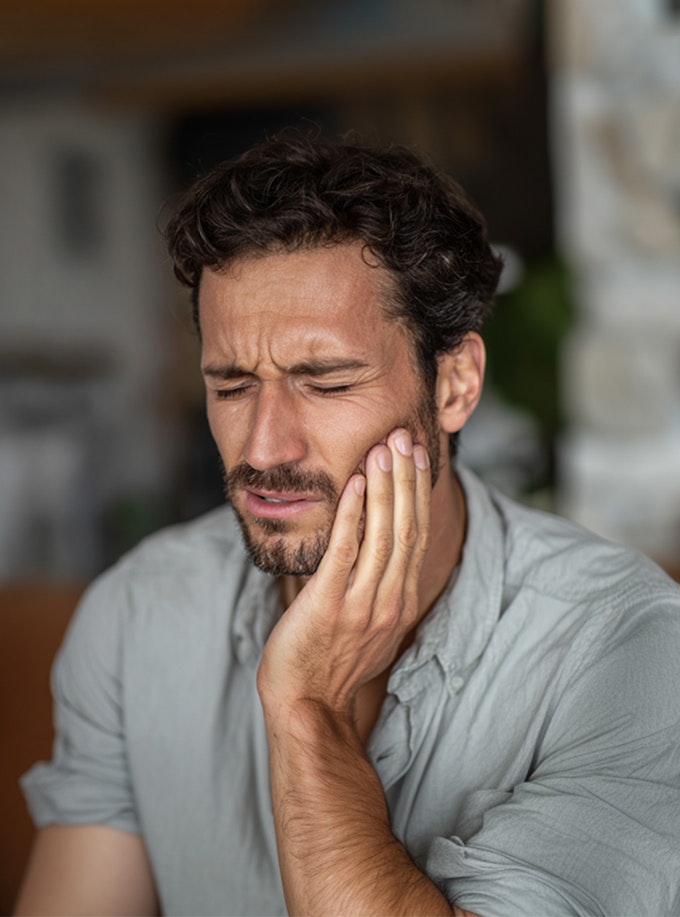 Man with a pained expression holding his cheek, indicating a possible toothache.