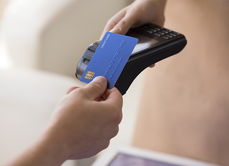 Hand holding a credit card being tapped on a payment terminal in a close‑up shot.