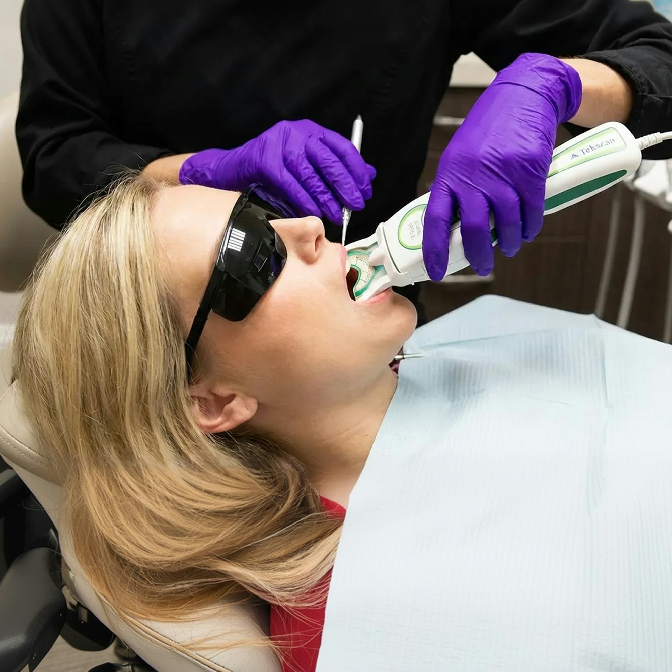 Patient undergoing TekScan bite analysis with dental assistant in purple gloves using handheld device