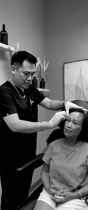 Dr. Charleston Chua examining a seated patient’s forehead and brow area during a consultation in a clinical setting.