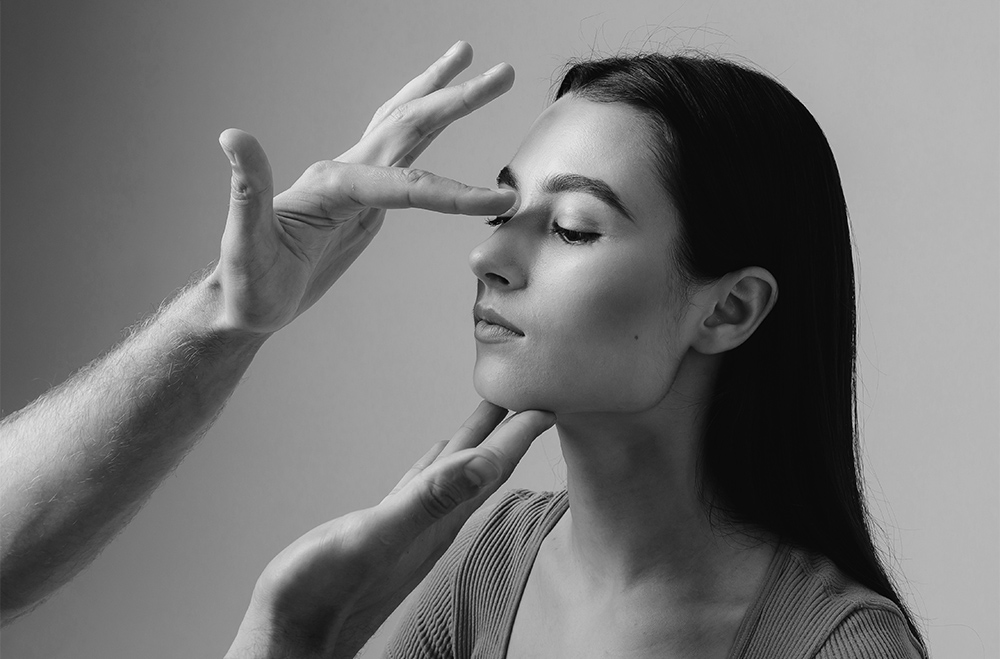 Clinician examining a woman’s nose by lightly pressing the bridge while supporting her chin during a cosmetic assessment.