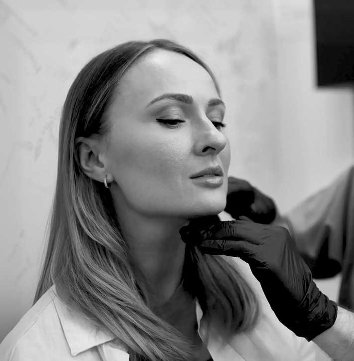 Clinician wearing black gloves gently examining woman’s jawline during a cosmetic consultation