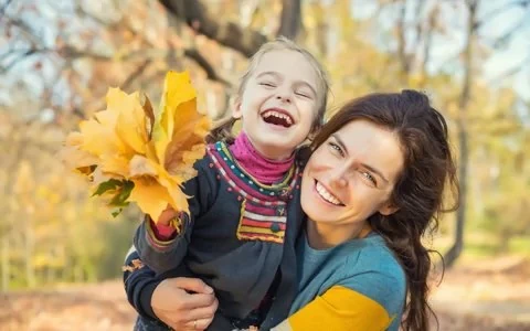 Laughing mom and daughter holding fall leaves