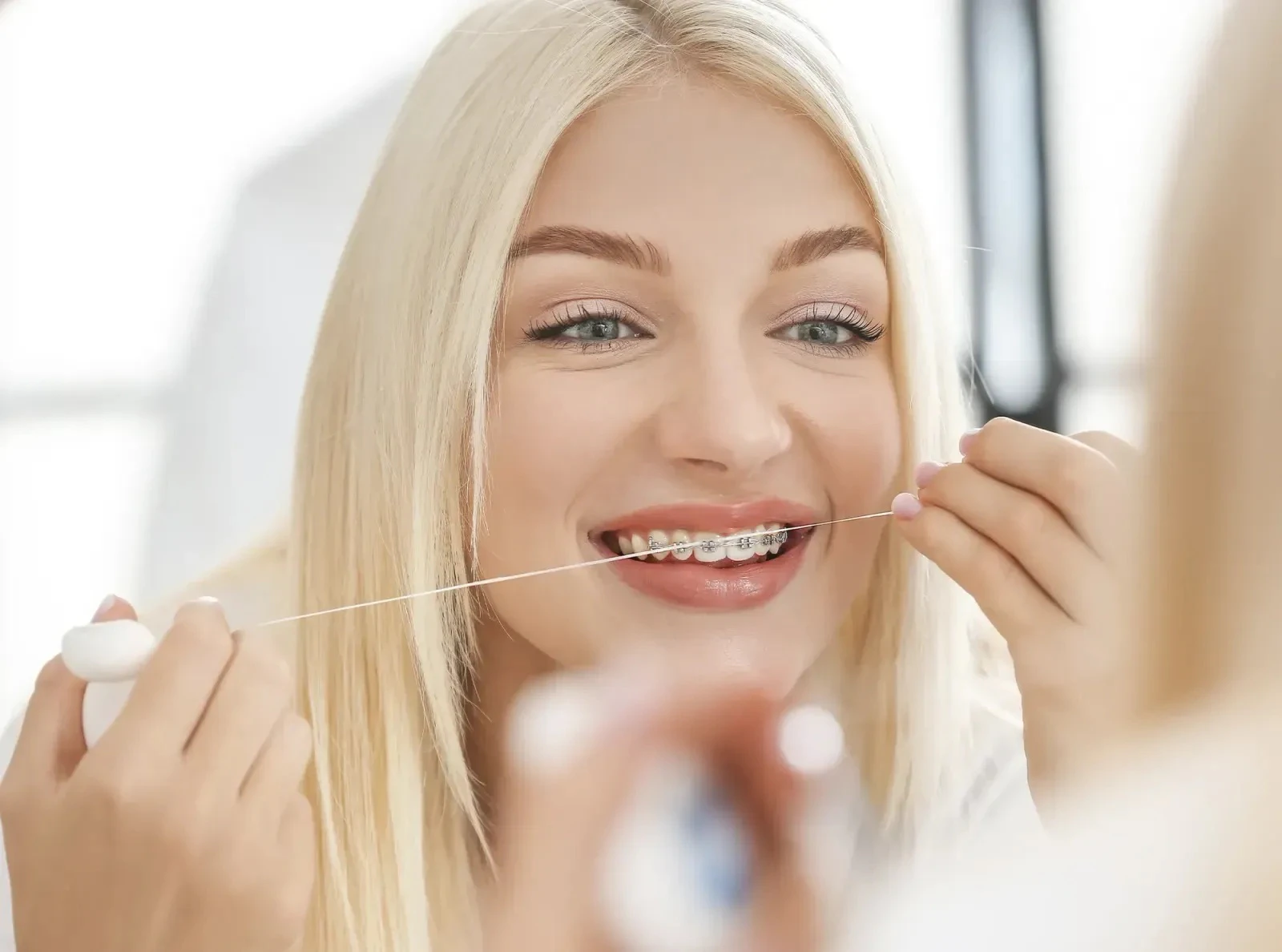 woman with braces flossing in mirror