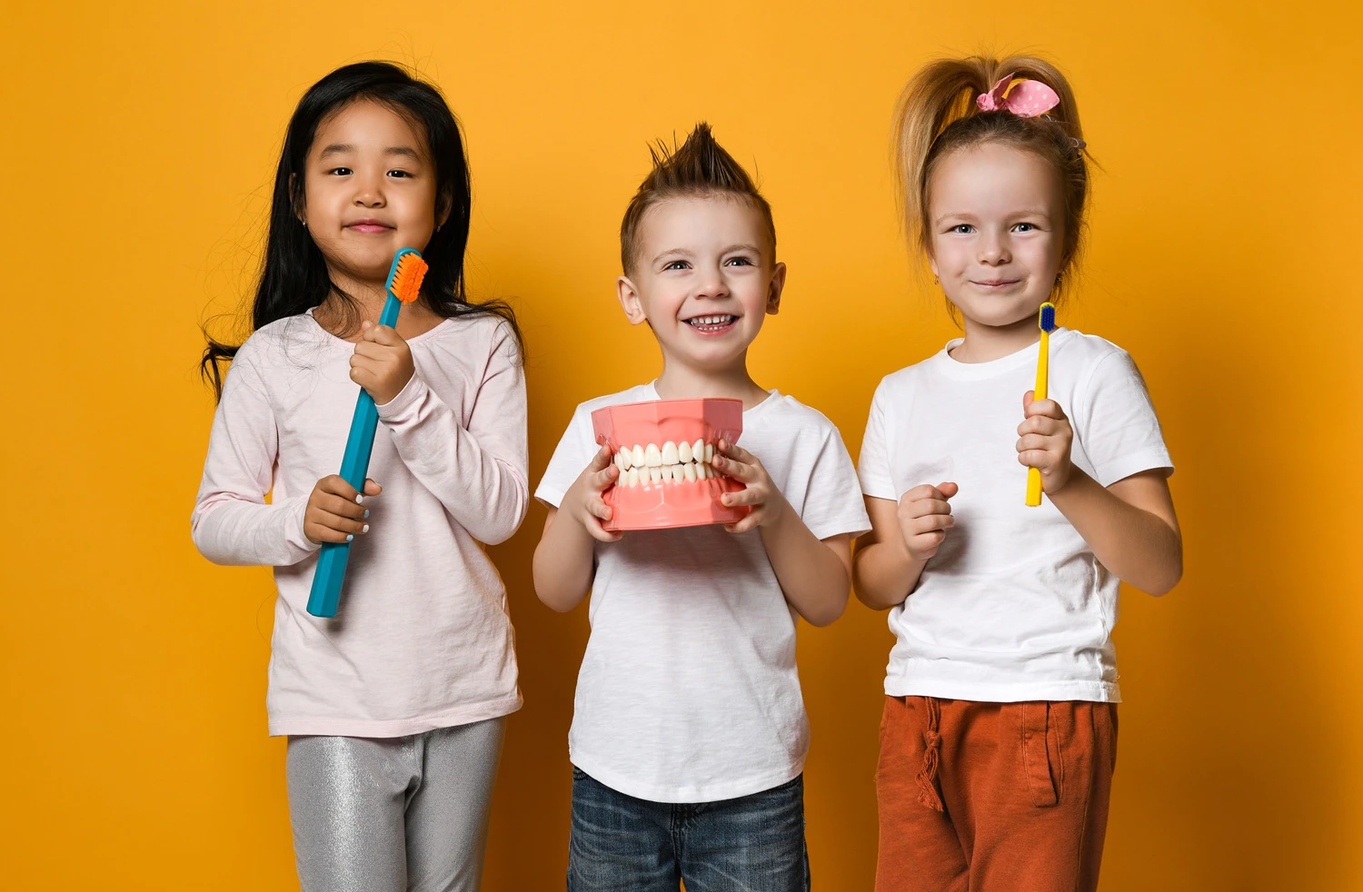 Smiling kids holding large toothbrushes and dental model