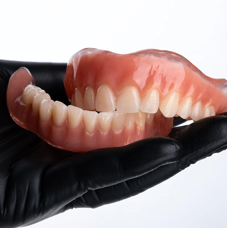 Dentures from VORA Dentistry in a gloved hand